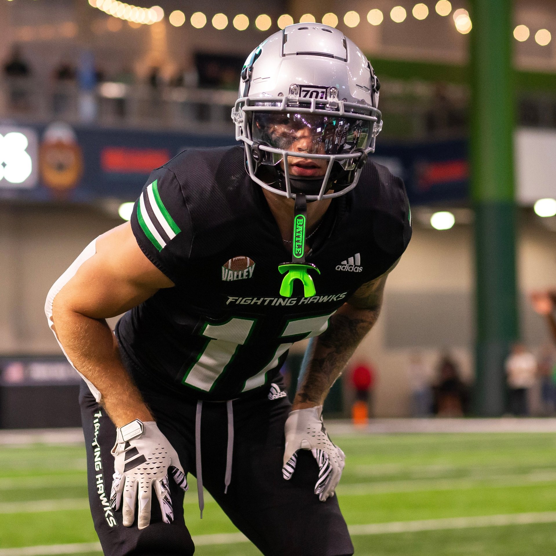Football player in black uniform with number 17 crouching in defensive stance on field under evening lights